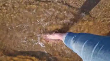 Çıplak kadın ayakları nehir sahilinde yürüyor, birinci şahıs manzaralı. Yazın nehrin yanında yürü. Kum ve suyun üzerinde yürüyen insan ayaklarının yakın çekimi. Yazın güzel havada yürü. Plaj