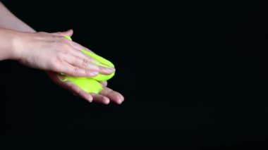 Kız yeşil balçık yoğuruyor. Kadının elleri siyah arka planda parlak yeşil bir balçığı birbirine yaklaştırıyor. Rahatlamak için stres önleyici oyuncak. Eğlenceli bir duyusal aktivite. Oyuncakçı konsepti