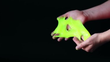 Kız yeşil balçık yoğuruyor. Kadının elleri siyah arka planda parlak yeşil bir balçığı birbirine yaklaştırıyor. Rahatlamak için stres önleyici oyuncak. Eğlenceli bir duyusal aktivite. Oyuncakçı konsepti