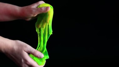 Kız yeşil balçık yoğuruyor. Kadının elleri siyah arka planda parlak yeşil bir balçığı birbirine yaklaştırıyor. Rahatlamak için stres önleyici oyuncak. Eğlenceli bir duyusal aktivite. Oyuncakçı konsepti