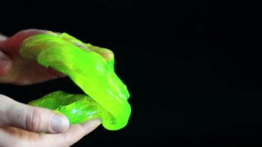 Kız yeşil balçık yoğuruyor. Kadının elleri siyah arka planda parlak yeşil bir balçığı birbirine yaklaştırıyor. Rahatlamak için stres önleyici oyuncak. Eğlenceli bir duyusal aktivite. Oyuncakçı konsepti