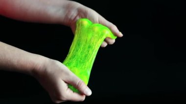 Kız yeşil balçık yoğuruyor. Kadının elleri siyah arka planda parlak yeşil bir balçığı birbirine yaklaştırıyor. Rahatlamak için stres önleyici oyuncak. Eğlenceli bir duyusal aktivite. Oyuncakçı konsepti