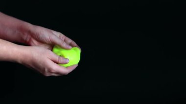 Kız yeşil balçık yoğuruyor. Kadının elleri siyah arka planda parlak yeşil bir balçığı birbirine yaklaştırıyor. Rahatlamak için stres önleyici oyuncak. Eğlenceli bir duyusal aktivite. Oyuncakçı konsepti