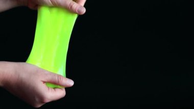 Kız yeşil balçık yoğuruyor. Kadının elleri siyah arka planda parlak yeşil bir balçığı birbirine yaklaştırıyor. Rahatlamak için stres önleyici oyuncak. Eğlenceli bir duyusal aktivite. Oyuncakçı konsepti