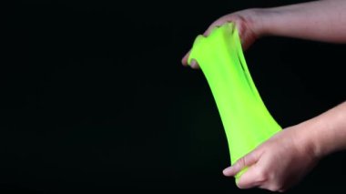 Kız yeşil balçık yoğuruyor. Kadının elleri siyah arka planda parlak yeşil bir balçığı birbirine yaklaştırıyor. Rahatlamak için stres önleyici oyuncak. Eğlenceli bir duyusal aktivite. Oyuncakçı konsepti