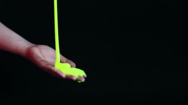 Kız yeşil balçık yoğuruyor. Kadının elleri siyah arka planda parlak yeşil bir balçığı birbirine yaklaştırıyor. Rahatlamak için stres önleyici oyuncak. Eğlenceli bir duyusal aktivite. Oyuncakçı konsepti