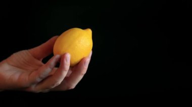 Olgun bir limonu tutan bir kadının yakın çekimi. Siyah arka planda sarı limon. Malzeme. Meyve ve yiyecek konsepti. Citrus.