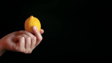 Olgun bir limonu tutan bir kadının yakın çekimi. Siyah arka planda sarı limon. Malzeme. Meyve ve yiyecek konsepti. Citrus.
