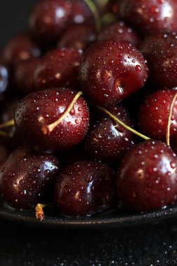 Siyah bir tabakta vişneli, ıslak arka planda, yakın plan. Islak tatlı olgun kirazlar. Yeşil saplı koyu kırmızı kirazlar ince su damlacıklarıyla kaplı. Yaz meyveleri, vitaminler