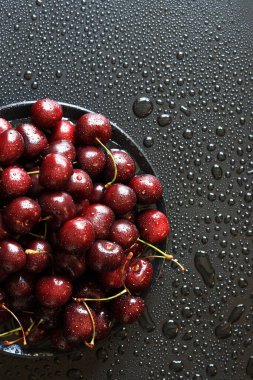 Siyah arka planda kiraz çilekleri, yakın plan. Islak tatlı olgun kirazlar. Yeşil saplı koyu kırmızı kirazlar ince su damlacıklarıyla kaplı. Yaz meyveleri, vitaminler. Arkaplan