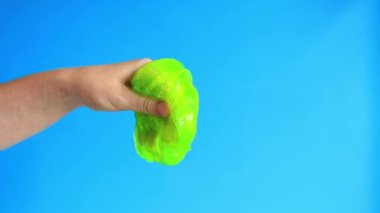 Kadının elleri mavi arka planda parlak yeşil bir balçığı birbirine yaklaştırıyor. Rahatlamak için stres önleyici oyuncak. Eğlenceli duyusal aktivite. Oyuncakçı konsepti. Kız yeşil balçık yoğuruyor.