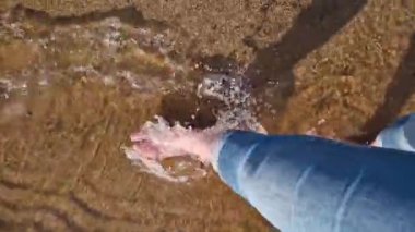 Çıplak kadın ayakları nehir sahilinde yürüyor. Yazın nehrin yanında yürü. Kum ve suyun üzerinde yürüyen insan ayaklarının yakın çekimi. Yazın güzel havada yürü. Plaj