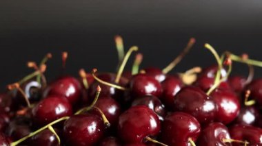 Siyah arka planda kiraz çilekleri, yakın plan. Tatlı kirazlar. Yeşil saplı koyu kırmızı kiraz, yan görüş. Yaz meyveleri, vitaminler