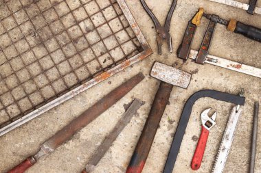 Beton arka planda eski inşaat aletleri, üst manzara. Çekiç, inşaat kıskacı, düz dosya, balyoz, el testeresi ve pense. Antika el aletleri koleksiyonu