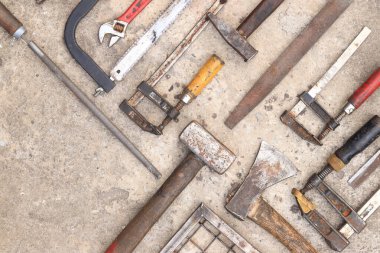 Beton arka planda eski inşaat aletleri, üst manzara. Çekiç, inşaat kıskacı, düz dosya, balyoz, el testeresi ve pense. Antika el aletleri koleksiyonu