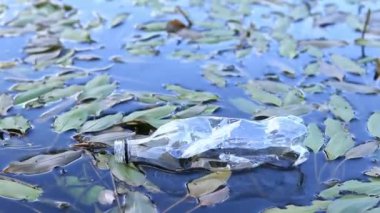 Plastik şişe suda, gölde ya da nehirde. Plastik kirliliği. Rezervlerin ve nehirlerin kirliliği. Nehirdeki çöpler yakın planda. Terk edilmiş bir şişe gölde yüzüyor. Nehir suyunda yiyecek plastiği