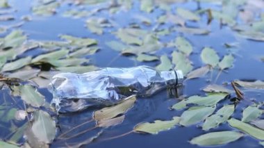 Plastik şişe suda, gölde ya da nehirde. Plastik kirliliği. Rezervlerin ve nehirlerin kirliliği. Nehirdeki çöpler yakın planda. Terk edilmiş bir şişe gölde yüzüyor. Nehir suyunda yiyecek plastiği