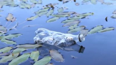 Plastik şişe suda, gölde ya da nehirde. Plastik kirliliği. Rezervlerin ve nehirlerin kirliliği. Nehirdeki çöpler yakın planda. Terk edilmiş bir şişe gölde yüzüyor. Nehir suyunda yiyecek plastiği