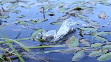 Plastik şişe suda, gölde ya da nehirde. Plastik kirliliği. Rezervlerin ve nehirlerin kirliliği. Nehirdeki çöpler yakın planda. Terk edilmiş bir şişe gölde yüzüyor. Nehir suyunda yiyecek plastiği