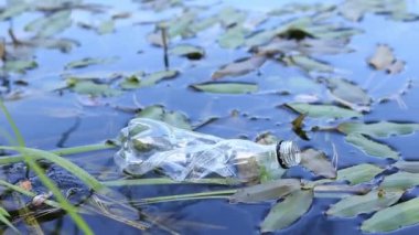 Plastik şişe suda, gölde ya da nehirde. Plastik kirliliği. Rezervlerin ve nehirlerin kirliliği. Nehirdeki çöpler yakın planda. Terk edilmiş bir şişe gölde yüzüyor. Nehir suyunda yiyecek plastiği
