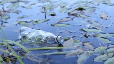 Plastik şişe suda, gölde ya da nehirde. Plastik kirliliği. Rezervlerin ve nehirlerin kirliliği. Nehirdeki çöpler yakın planda. Terk edilmiş bir şişe gölde yüzüyor. Nehir suyunda yiyecek plastiği