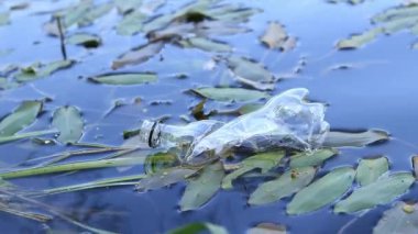 Plastik şişe suda, gölde ya da nehirde. Plastik kirliliği. Rezervlerin ve nehirlerin kirliliği. Nehirdeki çöpler yakın planda. Terk edilmiş bir şişe gölde yüzüyor. Nehir suyunda yiyecek plastiği