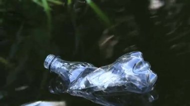 Plastik şişe suda, gölde ya da nehirde. Plastik kirliliği. Rezervlerin ve nehirlerin kirliliği. Nehirdeki çöpler yakın planda. Terk edilmiş bir şişe gölde yüzüyor. Nehir suyunda yiyecek plastiği