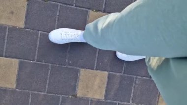 Beyaz spor ayakkabılı kadın bacakları, birinci şahıs görüşü. Yürüyüş ve yürüyüş. Kumaş pantolonlu insan bacakları ve sokakta yürüyen beyaz spor ayakkabılar. Beyaz ayakkabılar. 4K