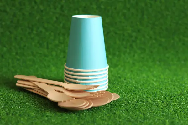 stock image Ecological dishes. Eco-friendly disposable tableware made of bamboo wood and paper on green grass background. Paper cups and disposable spoons and forks. Selective focus. Disposable tableware