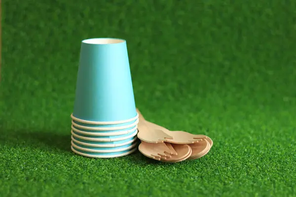 stock image Ecological dishes. Eco-friendly disposable tableware made of bamboo wood and paper on green grass background. Paper cups and disposable spoons and forks. Selective focus. Disposable tableware