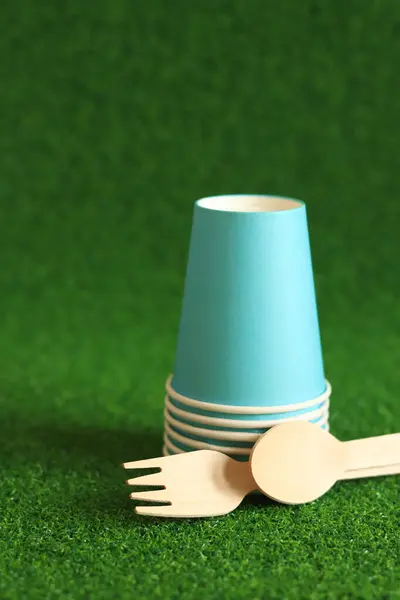 stock image Ecological dishes. Eco-friendly disposable tableware made of bamboo wood and paper on green grass background. Paper cups and disposable spoons and forks. Selective focus. Disposable tableware