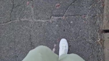 Beyaz spor ayakkabılı kadın bacakları, birinci şahıs görüşü. Yürüyüş ve yürüyüş. Kumaş pantolonlu insan bacakları ve sokakta yürüyen beyaz spor ayakkabılar. Beyaz ayakkabılar. 4K