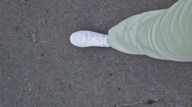 Beyaz spor ayakkabılı kadın bacakları, birinci şahıs görüşü. Yürüyüş ve yürüyüş. Kumaş pantolonlu insan bacakları ve sokakta yürüyen beyaz spor ayakkabılar. Beyaz ayakkabılar. 4K