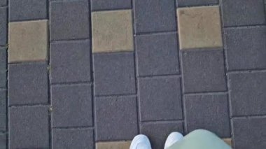 Beyaz spor ayakkabılı kadın bacakları, birinci şahıs görüşü. Yürüyüş ve yürüyüş. Kumaş pantolonlu insan bacakları ve sokakta yürüyen beyaz spor ayakkabılar. Beyaz ayakkabılar. 4K