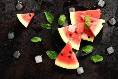 Nane ve buz küpleriyle siyah bir zeminde, sulu olgun karpuz dilimleri. Yukarıdan bak. Ferahlatıcı bir yaz meyvesi. Yaz limonatası için malzemeler. Lezzetli karpuz.