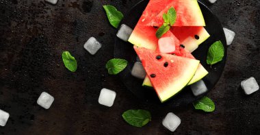 Nane ve buz küpleriyle siyah bir zeminde, sulu olgun karpuz dilimleri. Yukarıdan bak. Ferahlatıcı bir yaz meyvesi. Yaz limonatası için malzemeler. Lezzetli karpuz.