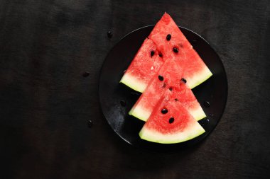 Sulu olgun karpuz dilimleri, siyah bir tabakta karpuz, siyah ahşap bir arka planda. Üst Manzara. Ferahlatıcı bir yaz meyvesi. Lezzetli karpuz.