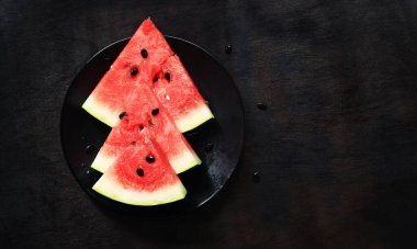 Sulu olgun karpuz dilimleri, siyah bir tabakta karpuz, siyah ahşap bir arka planda. Üst Manzara. Ferahlatıcı bir yaz meyvesi. Lezzetli karpuz.