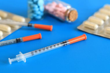 Mavi arka planda insülin şırıngaları ve vitaminler. Diyabet tedavisi. Tıp ve sağlık konsepti. Sağlık hizmetleri. İnsülin enjeksiyonları için kullanılmayan, tek kullanımlık şırıngalar. Vitaminler ve besin takviyeleri