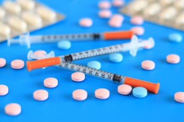Mavi arka planda insülin şırıngaları ve vitaminler. Diyabet tedavisi. Tıp ve sağlık konsepti. Sağlık hizmetleri. İnsülin enjeksiyonları için kullanılmayan, tek kullanımlık şırıngalar. Vitaminler ve besin takviyeleri