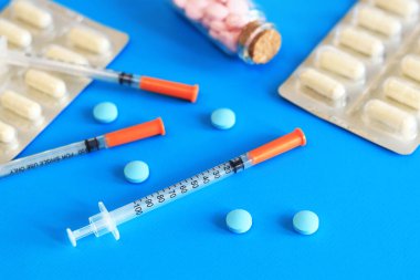 Mavi arka planda insülin şırıngaları ve vitaminler. Diyabet tedavisi. Tıp ve sağlık konsepti. Sağlık hizmetleri. İnsülin enjeksiyonları için kullanılmayan, tek kullanımlık şırıngalar. Vitaminler ve besin takviyeleri