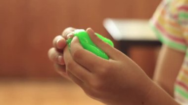 Küçük kız sümükle oynuyor. Parlak balçığı geren ellerin yakın çekimi. Eğlence ve oyun anlayışı, duyusal aktiviteler. Seçici odaklanma. Modaya uygun sıvı oyuncak ellere ve parmaklara yapışıyor.