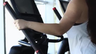 Spor salonunda, eliptik bir antrenörde egzersiz yapan bir kız. Spor kulübünde kardiyo eğitimi alan bir kız. Eliptik bir antrenörde eğitim, yakın plan. Spor yaşam tarzı. Sağlıklı yaşam tarzı kavramı