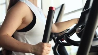 Spor salonunda, eliptik bir antrenörde egzersiz yapan bir kız. Spor kulübünde kardiyo eğitimi alan bir kız. Eliptik bir antrenörde eğitim, yakın plan. Spor yaşam tarzı. Sağlıklı yaşam tarzı kavramı