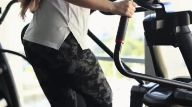 Spor salonunda, eliptik bir antrenörde egzersiz yapan bir kız. Spor kulübünde kardiyo eğitimi alan bir kız. Eliptik bir antrenörde eğitim, yakın plan. Spor yaşam tarzı. Sağlıklı yaşam tarzı kavramı