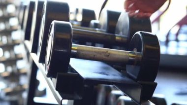 Kadın eli, vücut geliştirme. Salonda dambıllar var. Spor salonunda antreman yapmak için kadın elinin raftan dambılları çekişi. Fitness ekipmanlarıyla güçlü çalışma. Spor konsepti