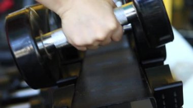 Kadın eli, vücut geliştirme. Salonda dambıllar var. Spor salonunda antreman yapmak için kadın eliyle dambılı askıya yerleştirirken yakın plan. Fitness ekipmanlarıyla güçlü çalışma. Spor konsepti