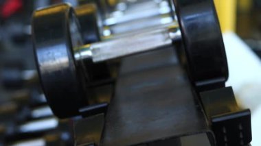 Kadın eli, vücut geliştirme. Salonda dambıllar var. Spor salonunda antreman yapmak için kadın eliyle dambılı askıya yerleştirirken yakın plan. Fitness ekipmanlarıyla güçlü çalışma. Spor konsepti