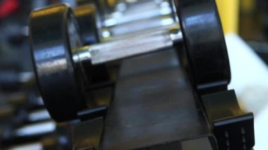 Kadın eli, vücut geliştirme. Salonda dambıllar var. Spor salonunda antreman yapmak için kadın eliyle dambılı askıya yerleştirirken yakın plan. Fitness ekipmanlarıyla güçlü çalışma. Spor konsepti