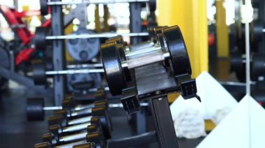 Kadın eli, vücut geliştirme. Salonda dambıllar var. Spor salonunda antreman yapmak için kadın eliyle dambılı askıya yerleştirirken yakın plan. Fitness ekipmanlarıyla güçlü çalışma. Spor konsepti